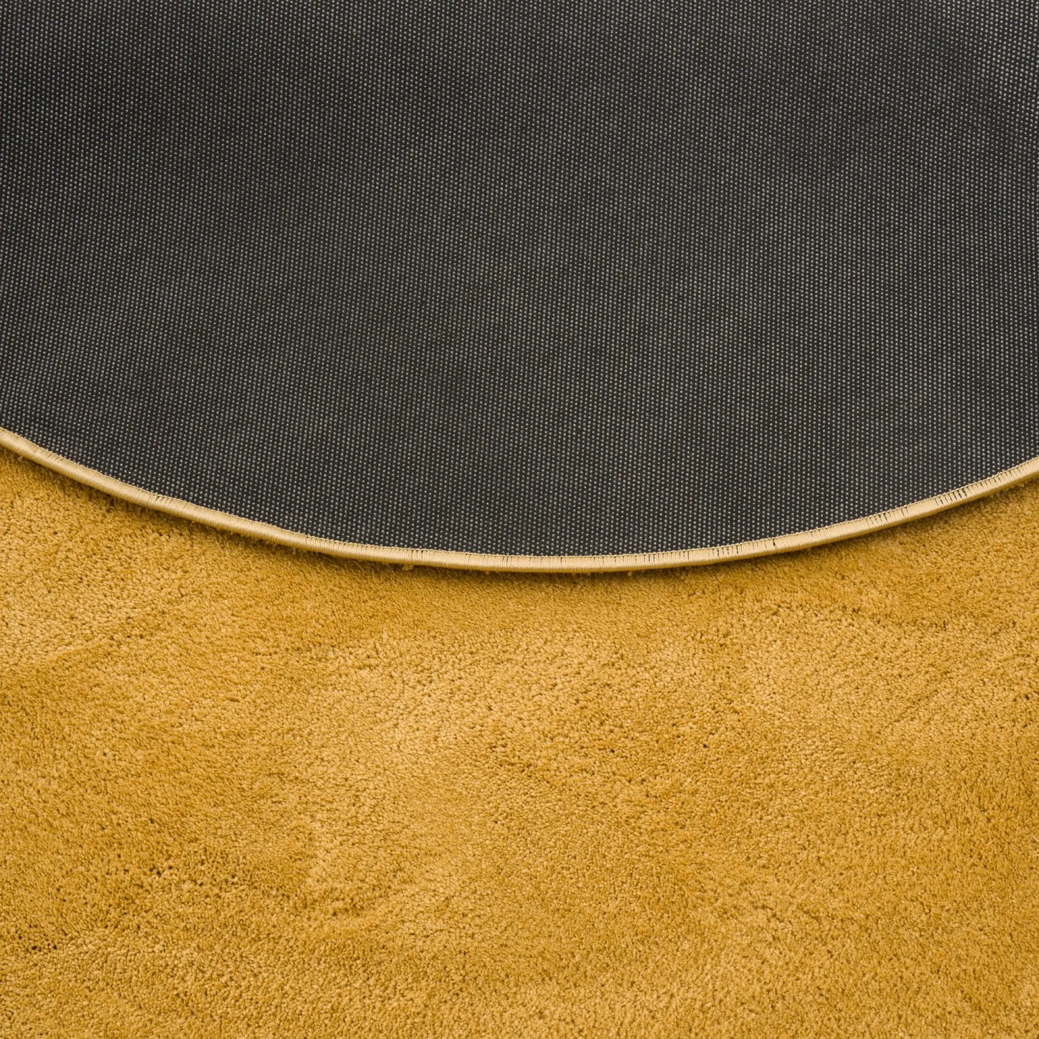 Detailansicht: Curryfarbener, runder Hochflor Teppich mit rutschfester Rückseite.