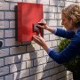 Frau befestigt Hausnummer mit Tesa Montageband auf Mauerwerk.