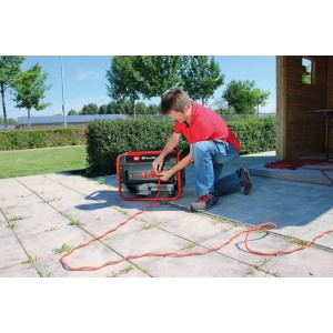 Mann schließt Kabel an rotes Einhell Notstromaggregat im Garten an. Mobiler Benzin-Stromerzeuger für Outdoor-Einsatz.