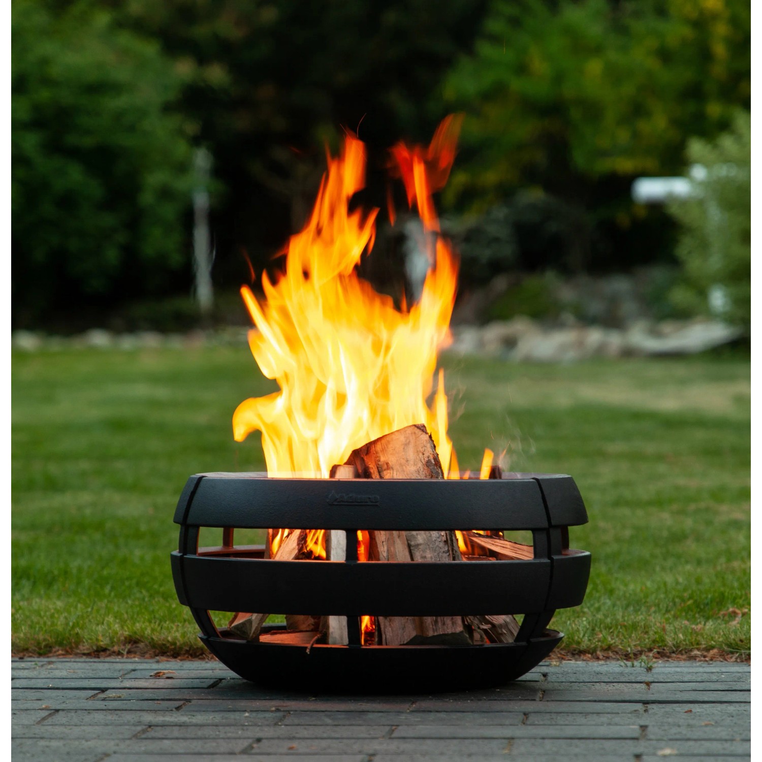 Aduro Feuerball aus Gusseisen mit Grillfunktion und brennendem Holz im Garten.