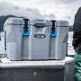 Dunkelgraue Kühlbox aus Kunststoff mit Tragegriffen und blauen Akzenten auf einem Boot.