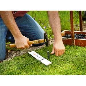 Gardena Mähroboter-Begrenzungskabel Installation mit Hammer und Hering im Garten.