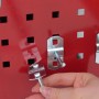 Hand befestigt silbernen Haken an rotem Lochraster des PROREGAL Werkstattwagens. Flexible Werkzeugaufhängung.