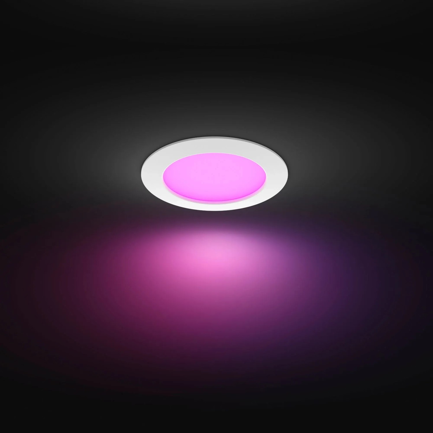 Weißer Philips Hue Einbauspot Slim mit farbigem Licht an dunkler Decke.
