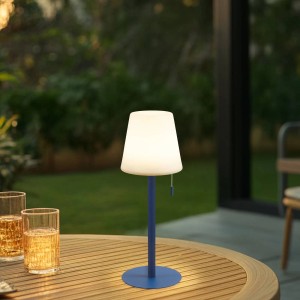 Blaue Lindby LED Azalea Tischleuchte auf Holztisch im Garten. Spritzwassergeschützte Außenleuchte aus Aluminium mit weißem Schirm.