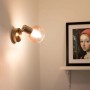 Goldener QAZQA Art Deco Aufbauspot Vidro mit rosa Glas, leuchtend an weißer Wand. Ideal für Wohnzimmer.