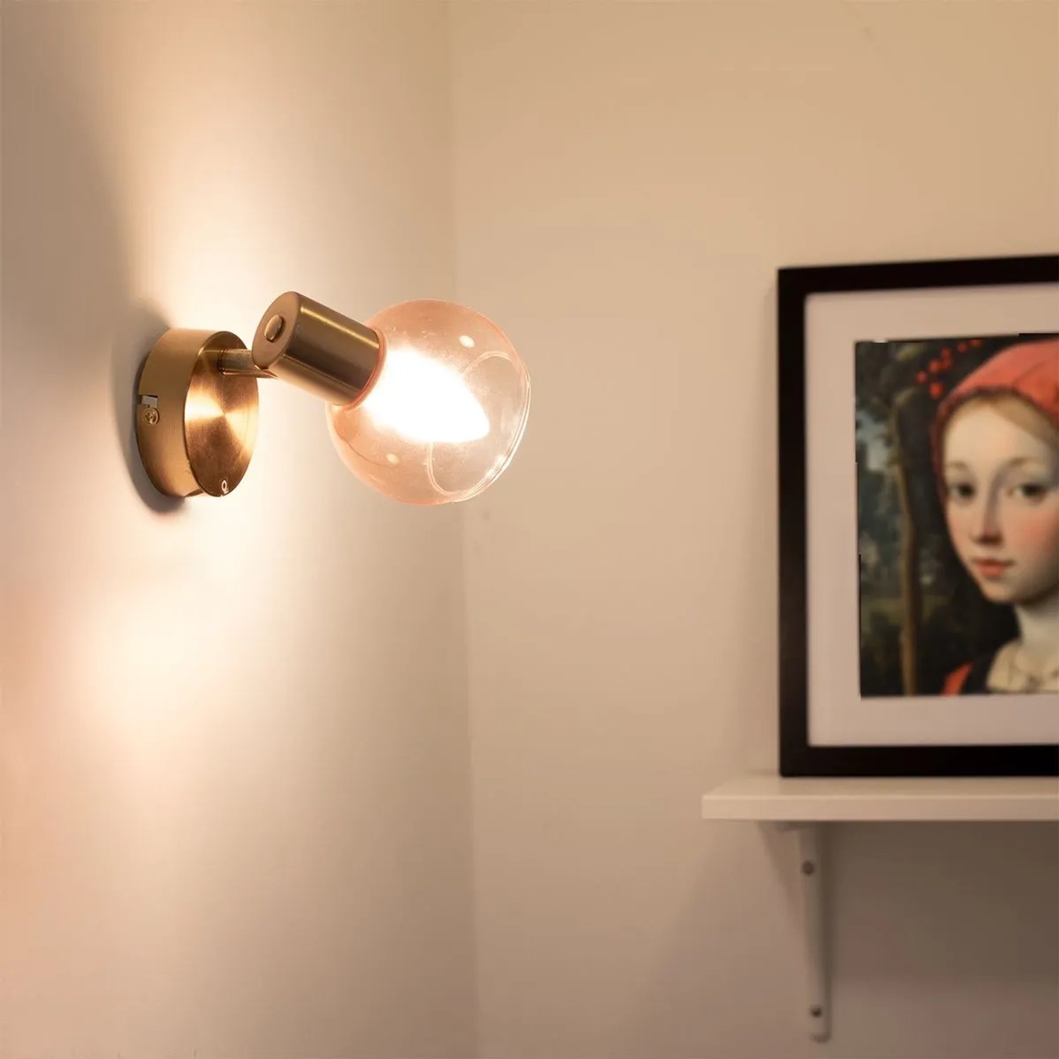 Goldener QAZQA Art Deco Aufbauspot Vidro mit rosa Glas, leuchtend an weißer Wand. Ideal für Wohnzimmer.