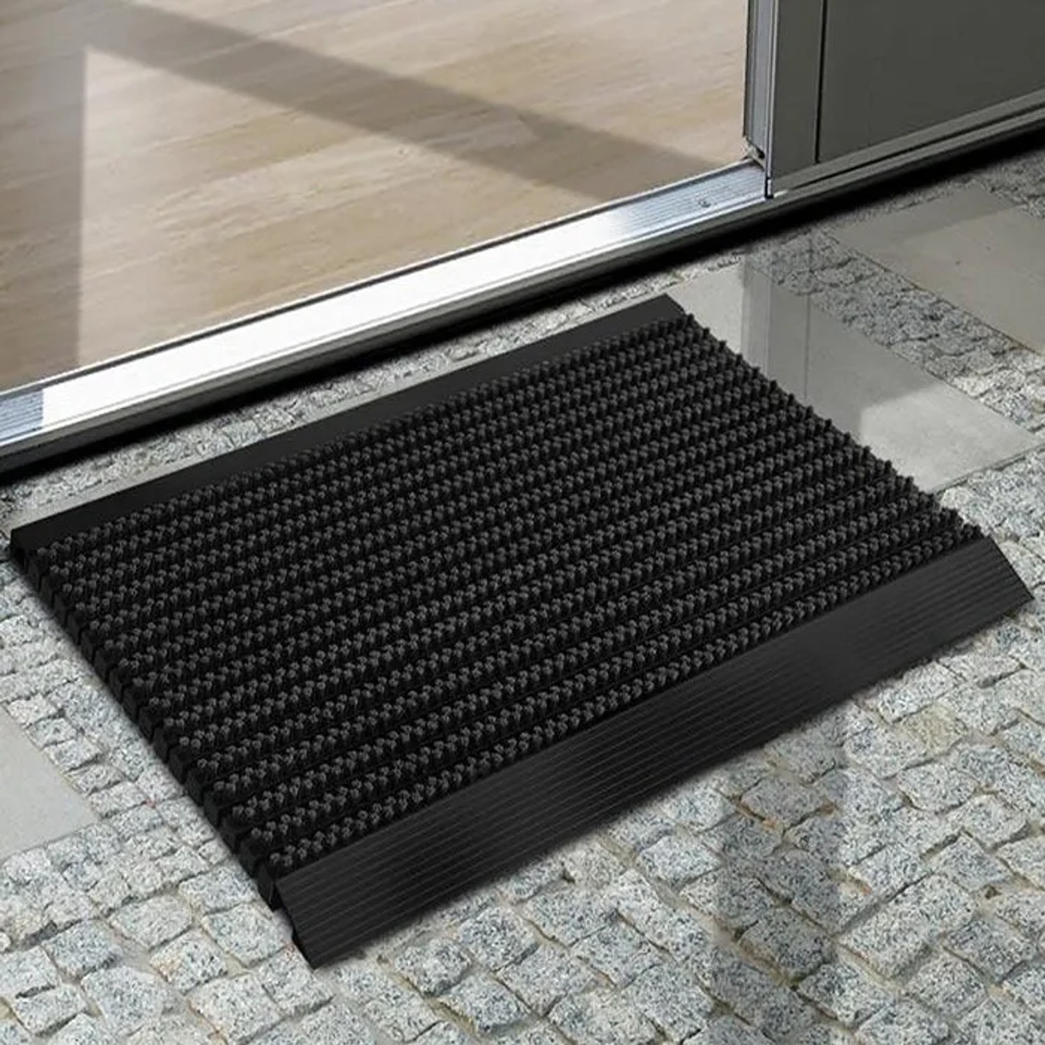 Schwarze Karat Fußmatte Power Brush 40x60 cm vor einer Tür. Fußabtreter mit Bürsten.