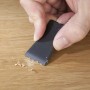 Hand glättet mit schwarzem Werkzeug eine Reparaturstelle auf hellem Laminat- oder Parkettboden. Westfalia Reparatur-Set.