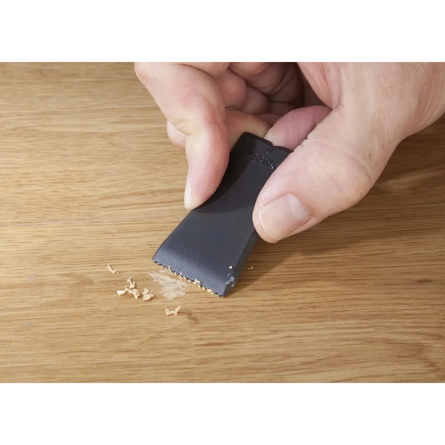 Hand glättet mit schwarzem Werkzeug eine Reparaturstelle auf hellem Laminat- oder Parkettboden. Westfalia Reparatur-Set.