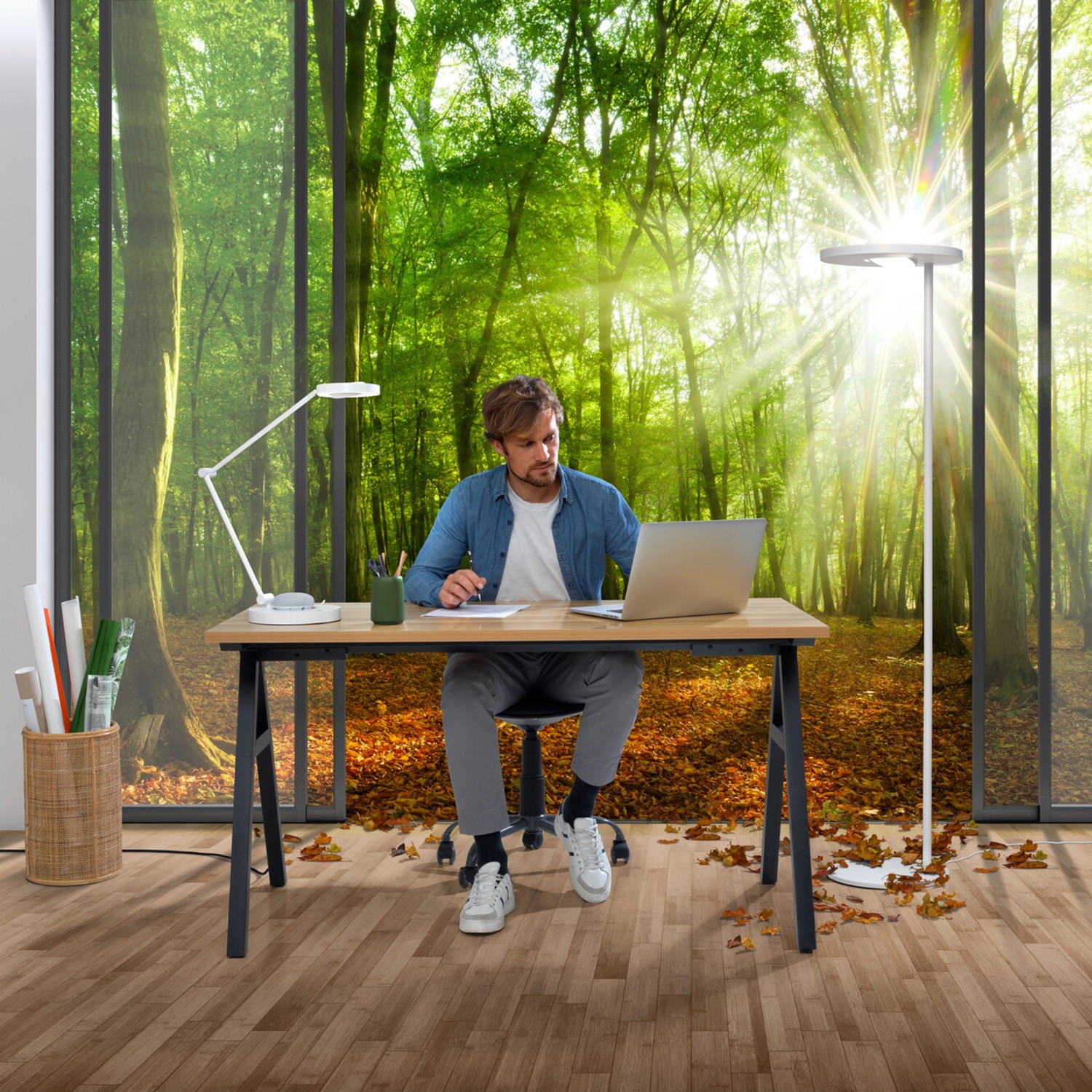 Mann arbeitet am Schreibtisch mit Ledvance Sun@Home Tischlampe und Stehlampe vor Waldtapete.