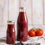 Dr. Oetker Smoothie Flasche (750ml) aus Glas, gefüllt mit rotem Smoothie, neben Blaubeeren und Tomaten.
