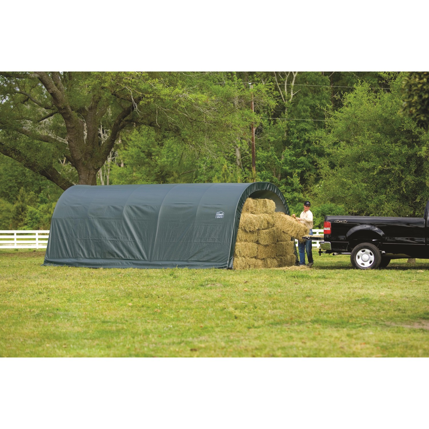 Grünes ShelterLogic Weidezelt (22,57 m²) mit Heu und Person beim Beladen eines Pickups.