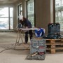 Blaue Garant Kabeltrommel 25m IP44 auf Baustelle. Arbeiterin nutzt sie für Gewerbe & Außenbereich.