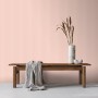 Rosa Vliestapete mit feinem Streifenmuster an einer Wand, dekoriert mit Holzbank und Vase. Sanders & Sanders Tapete.