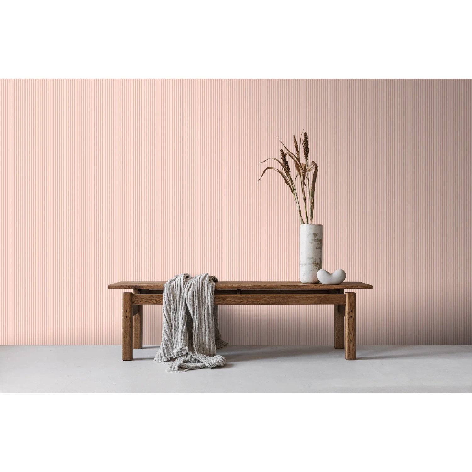 Rosa Vliestapete mit feinem Streifenmuster an einer Wand, dekoriert mit Holzbank und Vase. Sanders & Sanders Tapete.