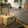 Geöffnete, sandfarbene Petromax Kühlbox 25l mit Eis und Getränken auf einer Holzterrasse.