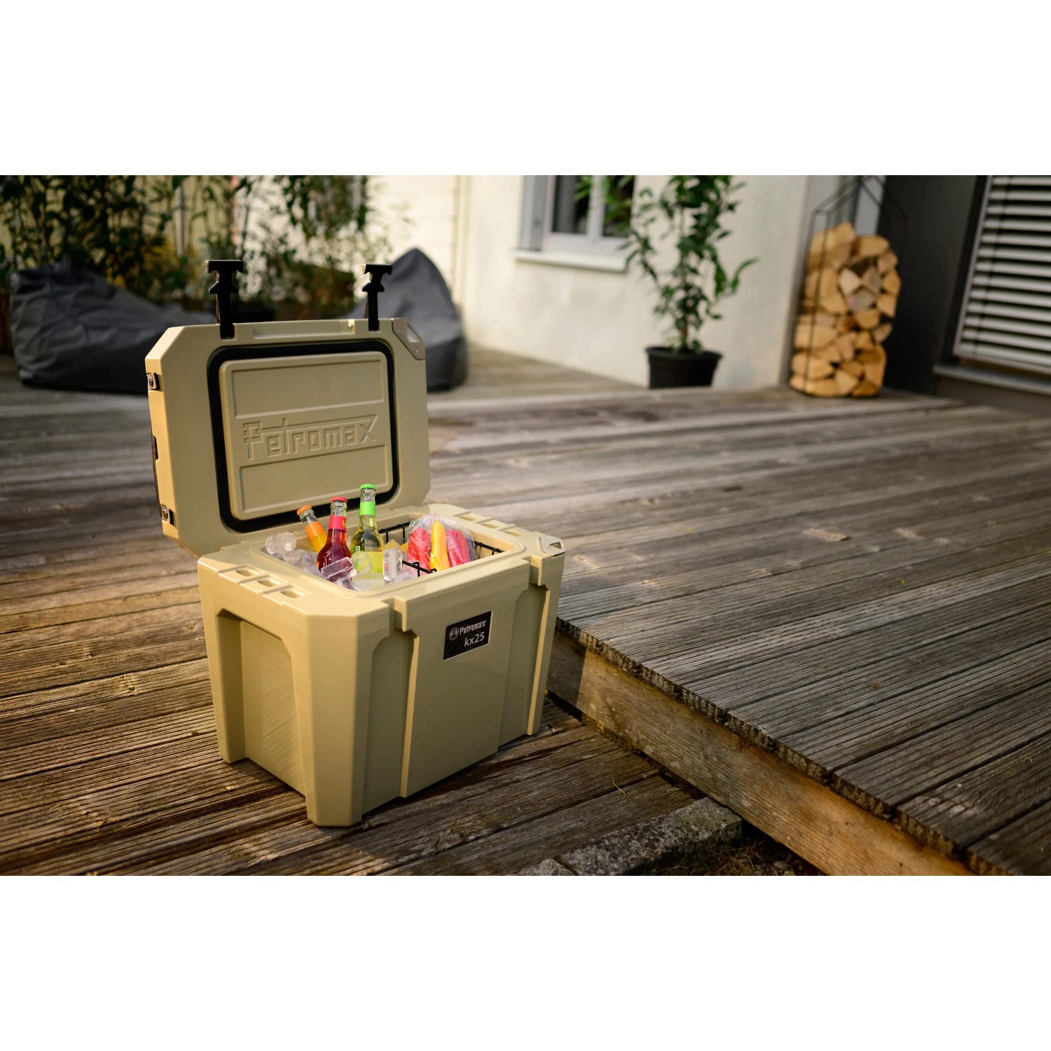 Geöffnete, sandfarbene Petromax Kühlbox 25l mit Eis und Getränken auf einer Holzterrasse.