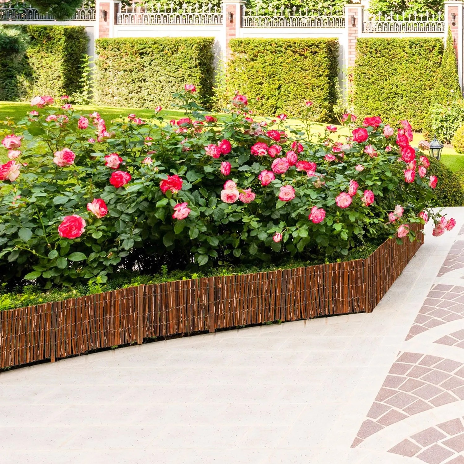 Flexible Weiden-Beeteinfassung, 20 cm hoch, trennt Rosenbeet mit pinken Blüten vom Gartenweg.