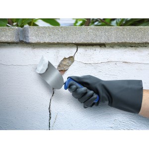 Auftragen von OBI Außenspachtel Weiß auf eine Wand mit Rissen und Löchern.