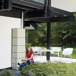 4rain Slim Regenwassertank in Sandbeige mit Zubehör und Frau mit Gießkanne.