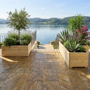Zwei massive HolzFee Pflanzkästen Dona aus Fichtenholz auf einer Terrasse am See, bepflanzt. Ideal für Garten & Balkon.