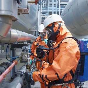 Zwei Personen in orangefarbenen Schutzanzügen und Dräger Atemschutzmasken arbeiten in einer Industrieanlage an Rohren.