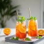 Zwei Gläser Aperol-Spritz mit Eis, Orangenscheiben und Minze auf einem grauen Tablett.