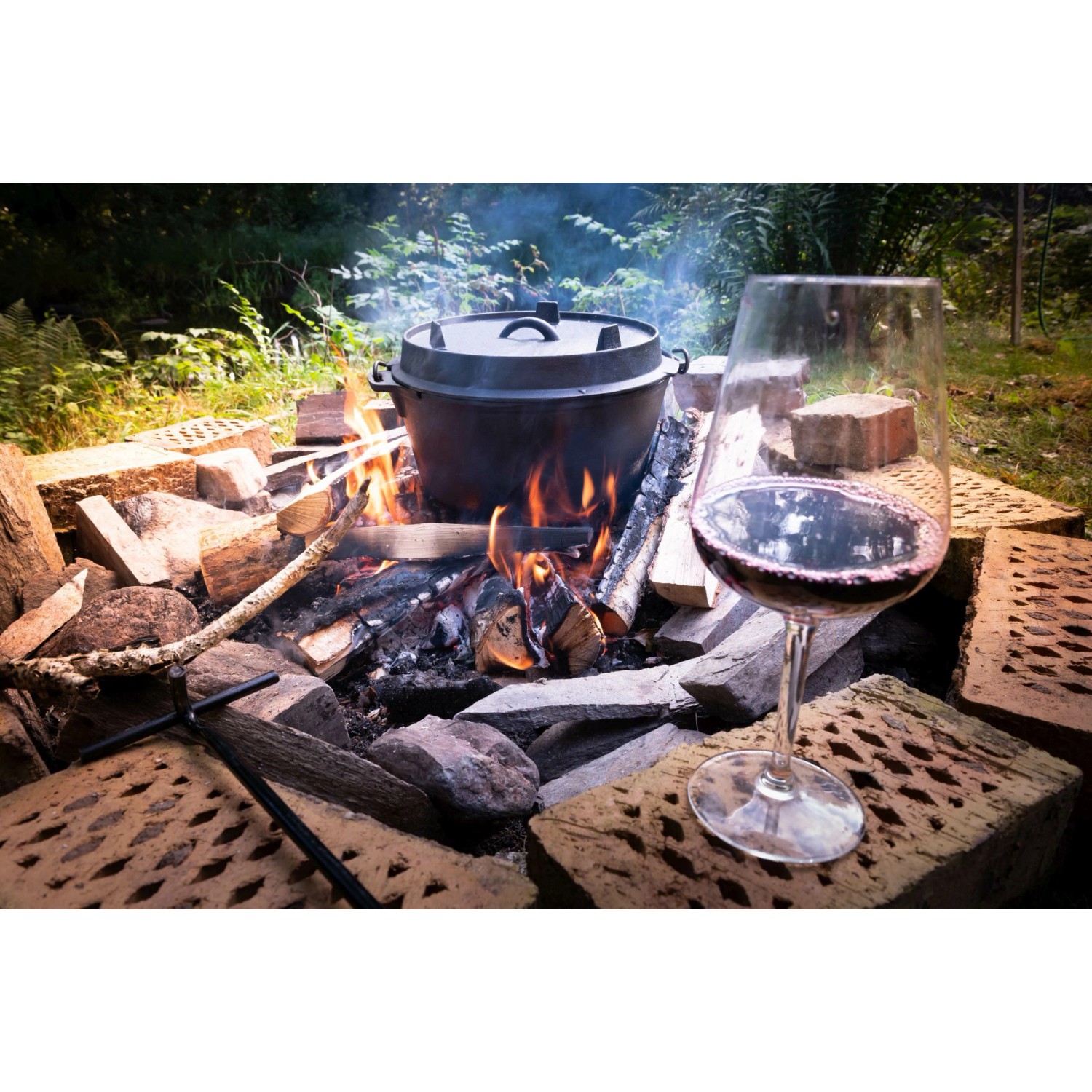 El Fuego Dutch Oven (7,2 l) aus Gusseisen über offenem Feuer mit Weinglas. Grillutensil für Outdoor-Küche.