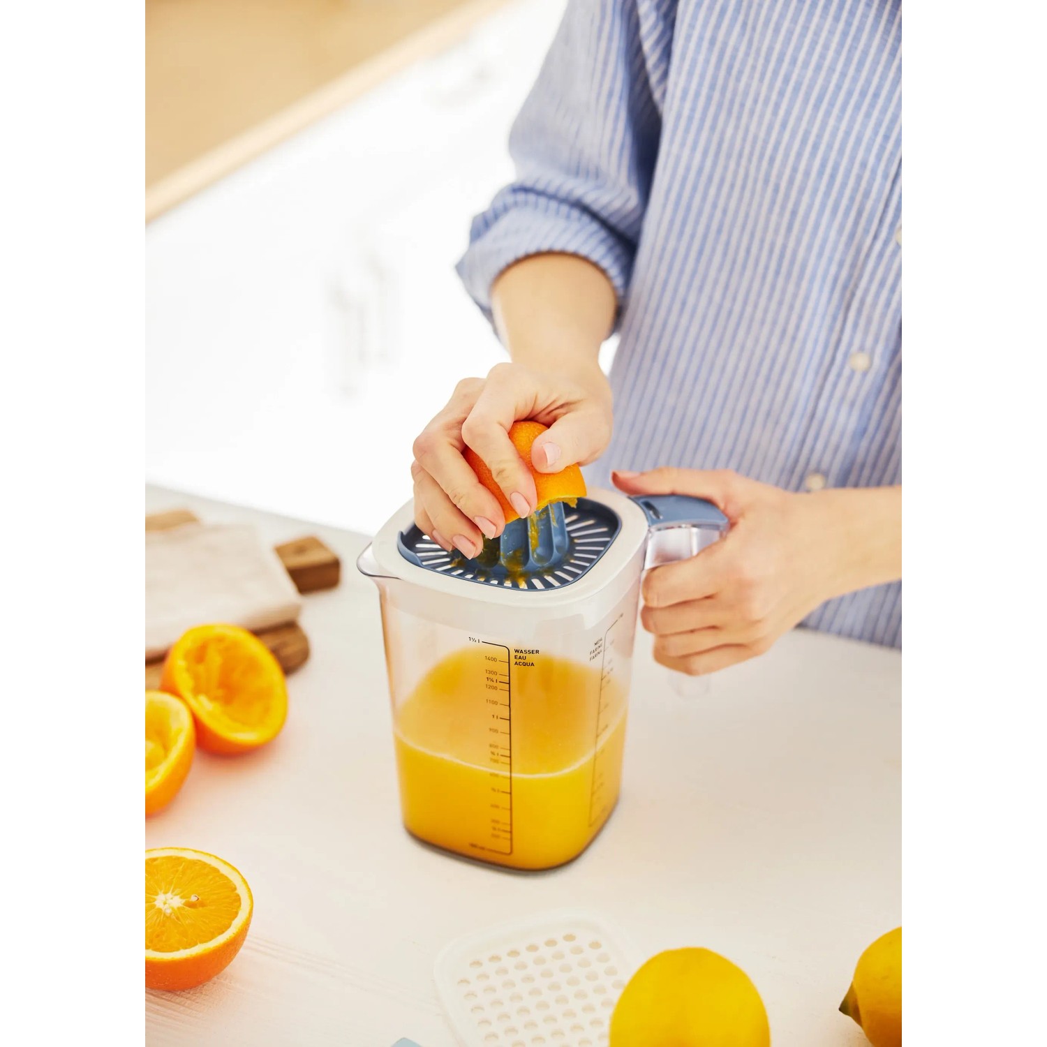 Rotho Messbecher Loft: Frau presst Orange mit Zitruspresse Aufsatz. Küchenhelfer transparent/blau.