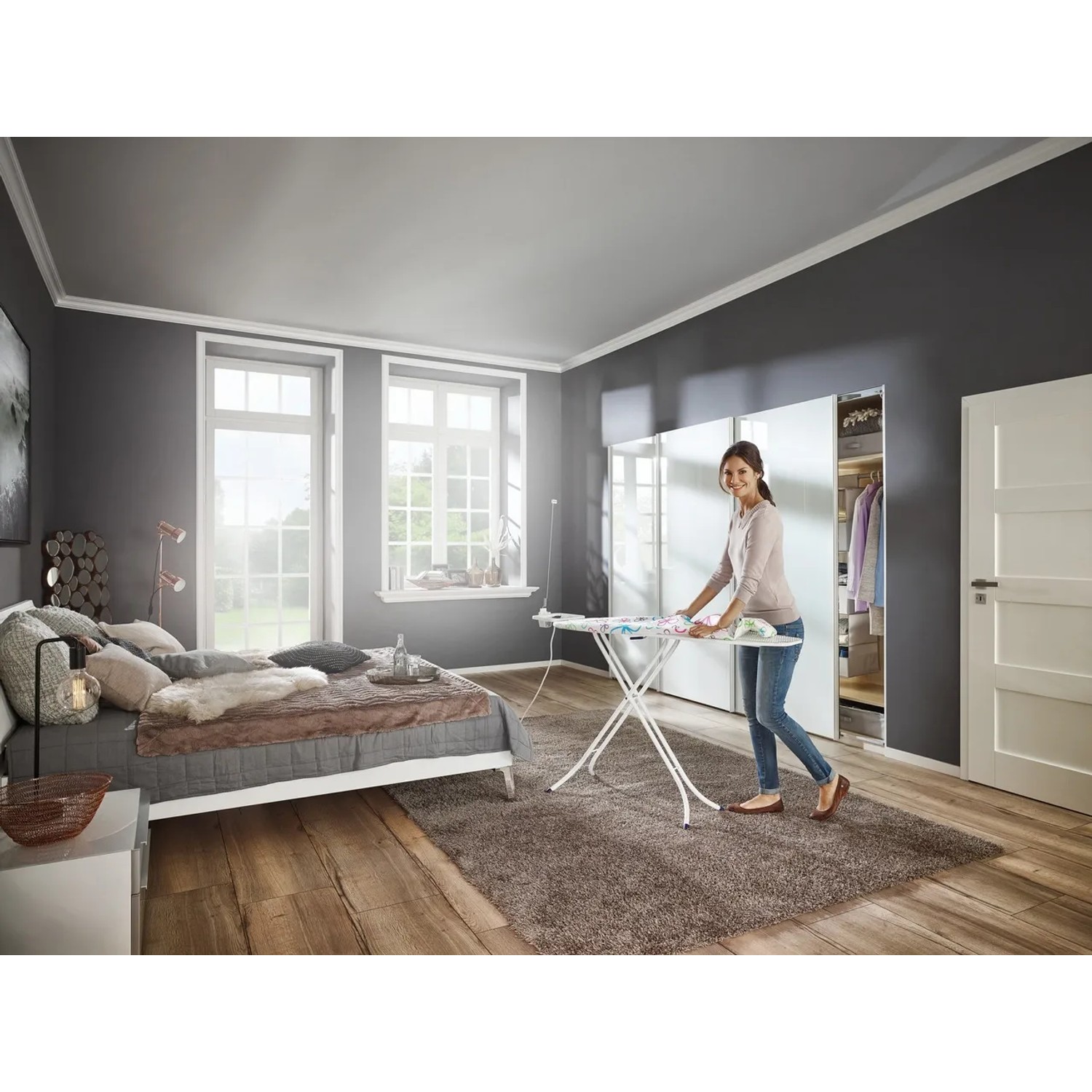 Frau bügelt Wäsche auf dem Leifheit Bügeltisch Fashion M Plus im Schlafzimmer.