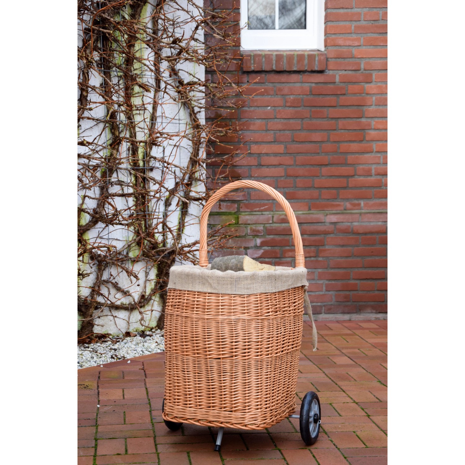 Kaminholzwagen aus Weide mit Jute-Auskleidung und Rädern vor einer Hauswand.