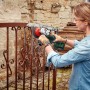 Frau schleift Metallzaun mit Bosch Akku-Winkelschleifer Universal Grind 18V-75. 