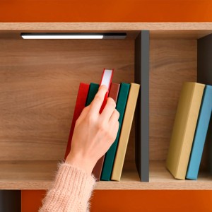 Schwarze Emuca LED-Wandleuchte mit Bewegungssensor unter Holzregal. Beleuchtet Bücher in Schränken. L600 mm, wiederaufladbar.