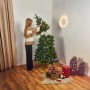 Frau setzt grüne Kunsttanne Nagano (150 cm) zusammen. Weihnachtsbaum mit Deko im Wohnzimmer.