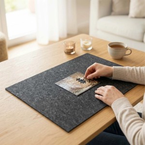 Graues Filz Puzzlebrett auf Holztisch. Person legt Puzzleteil. Stabile Unterlage für kreatives Puzzeln.