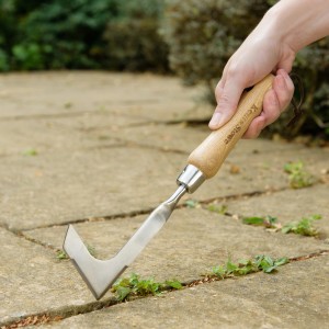 Kent & Stowe Fugenkratzer im Einsatz: Hand führt Werkzeug zum Entfernen von Unkraut zwischen Pflastersteinen.
