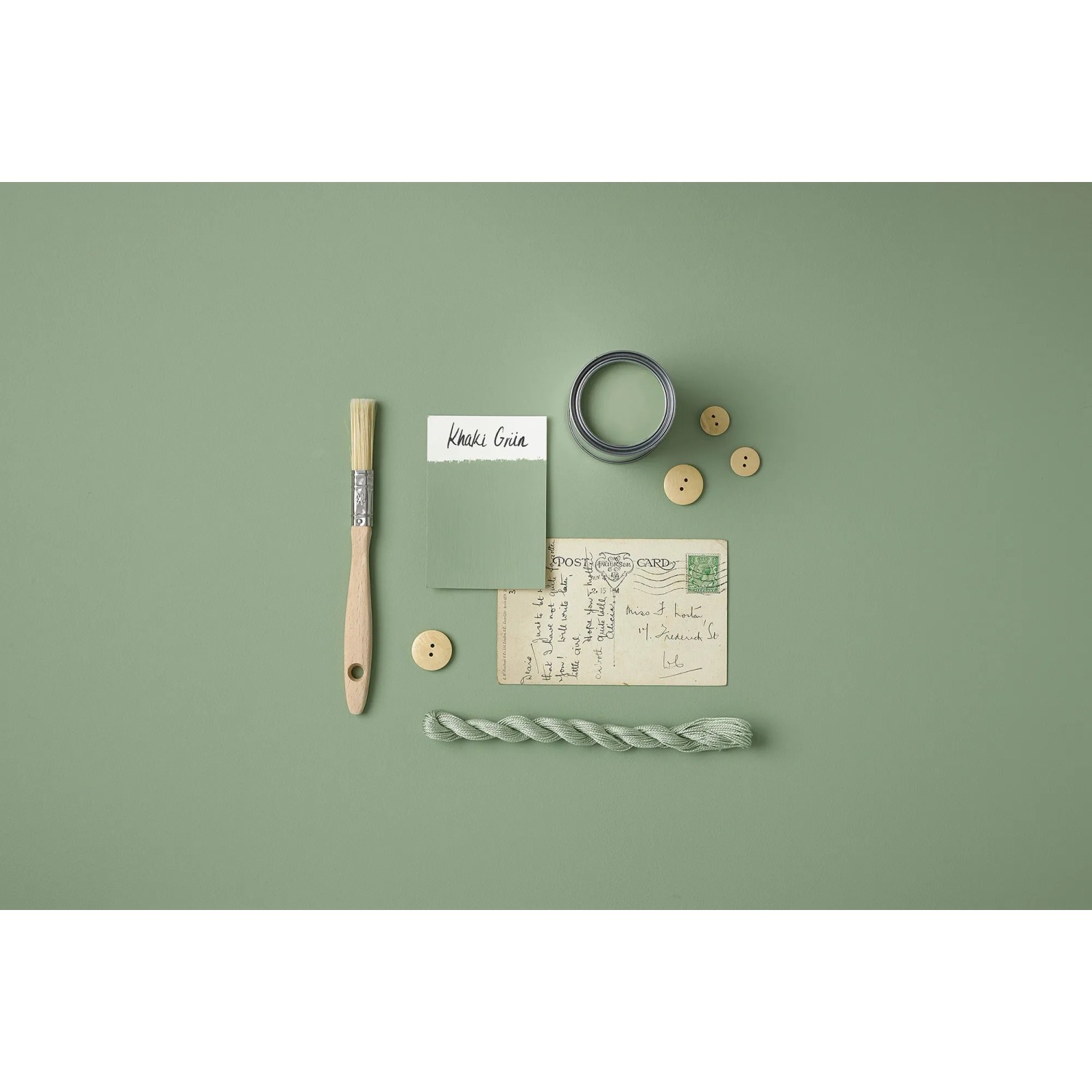 Rust-Oleum Kreidefarbe Khaki Grün matt, mit Pinsel, Farbmuster, Knöpfen und Postkarte auf farbigem Untergrund.