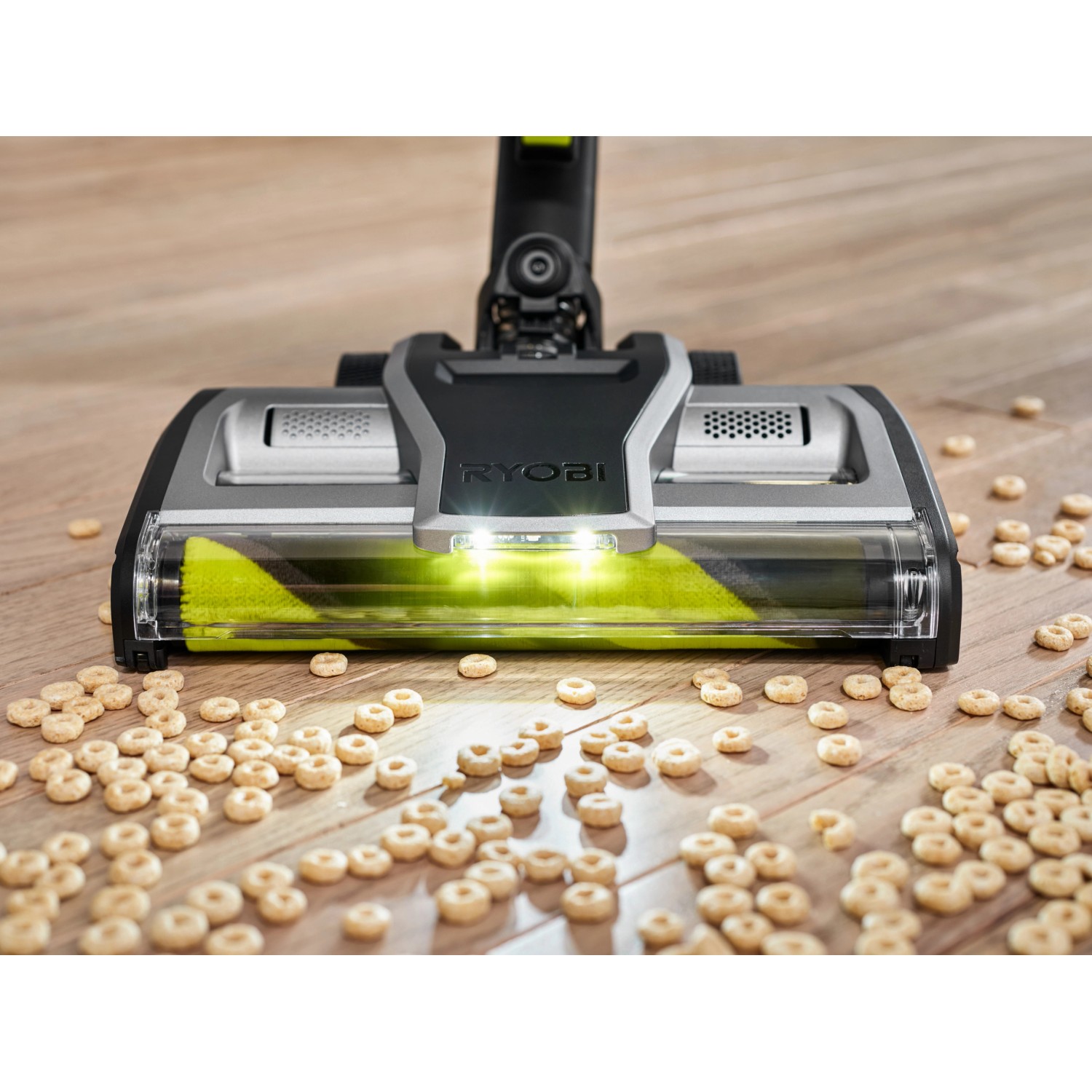 Ryobi Akku-Staubsauger RASV18BL-0 mit LED-beleuchteter Bodendüse beim Aufsaugen von Frühstücksflocken auf Holzboden.
