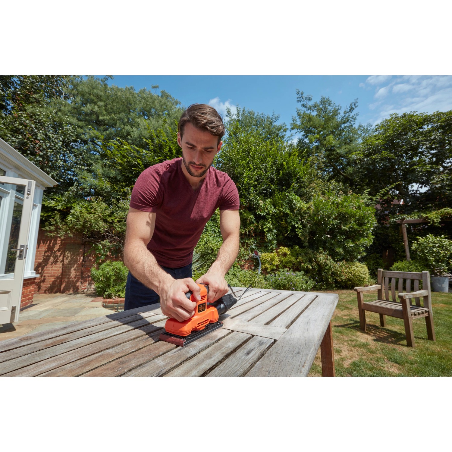 Mann schleift Tisch mit Black+Decker Schwingschleifer BEW220. Schleifmaschine in Orange und Schwarz.