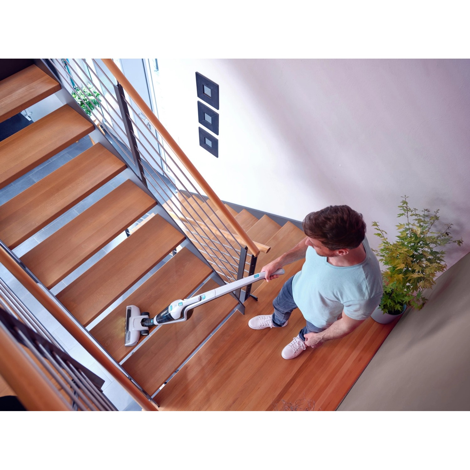 Mann saugt Treppe mit Leifheit Akku-Staubsauger Rotaro. Reinigungsgerät mit Akku-Handsauger.