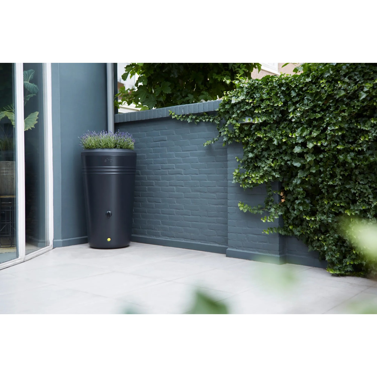 Schwarze Elho Regentonne Green-Basics 200L mit integriertem Blumentopf im Garten.