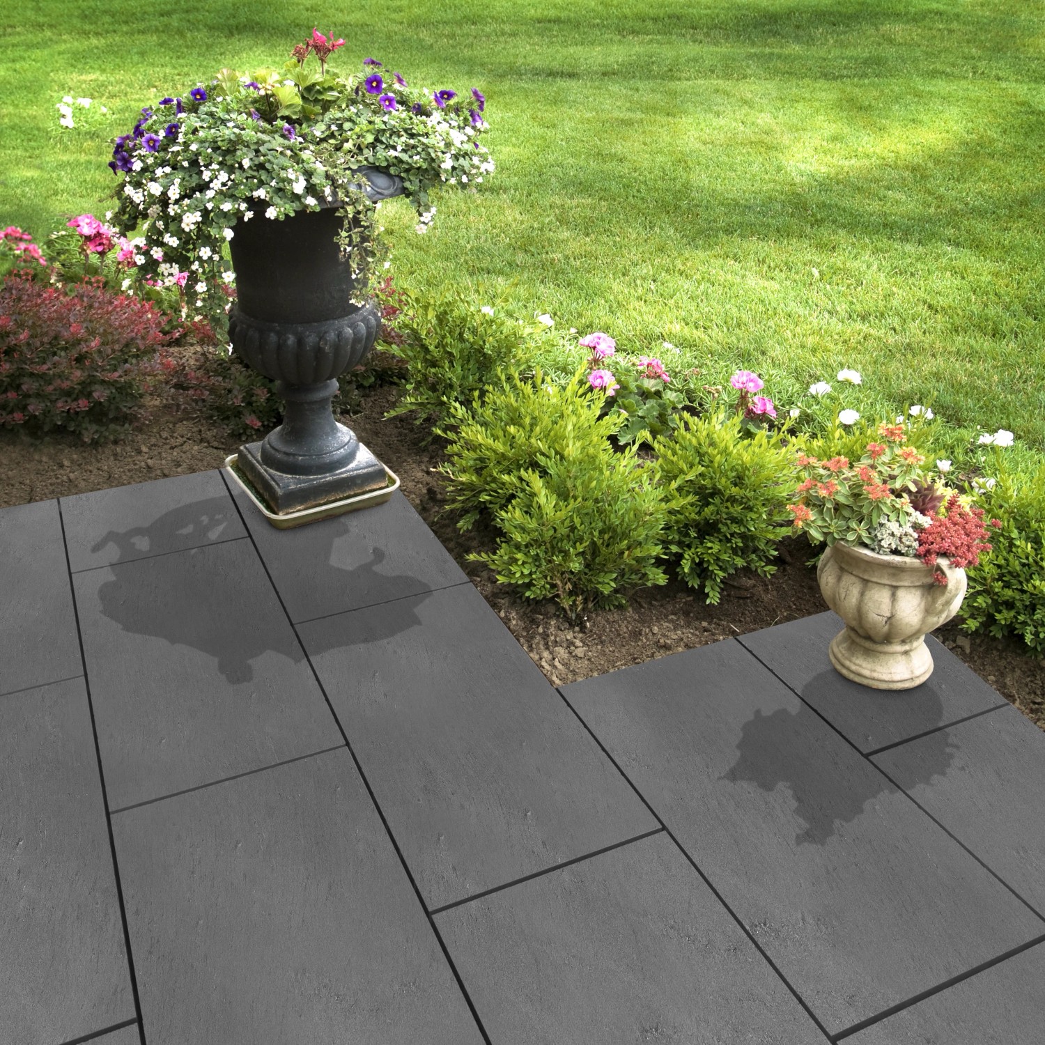 Verlegte, graue Florco Naturstein Klickfliese Stone Schiefer XL auf einer Terrasse mit Blumen.
