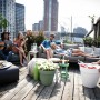 Elho Blumentopf Loft Urban, pistaziengrün, mit Rollen, auf einer Dachterrasse mit entspannten Menschen.