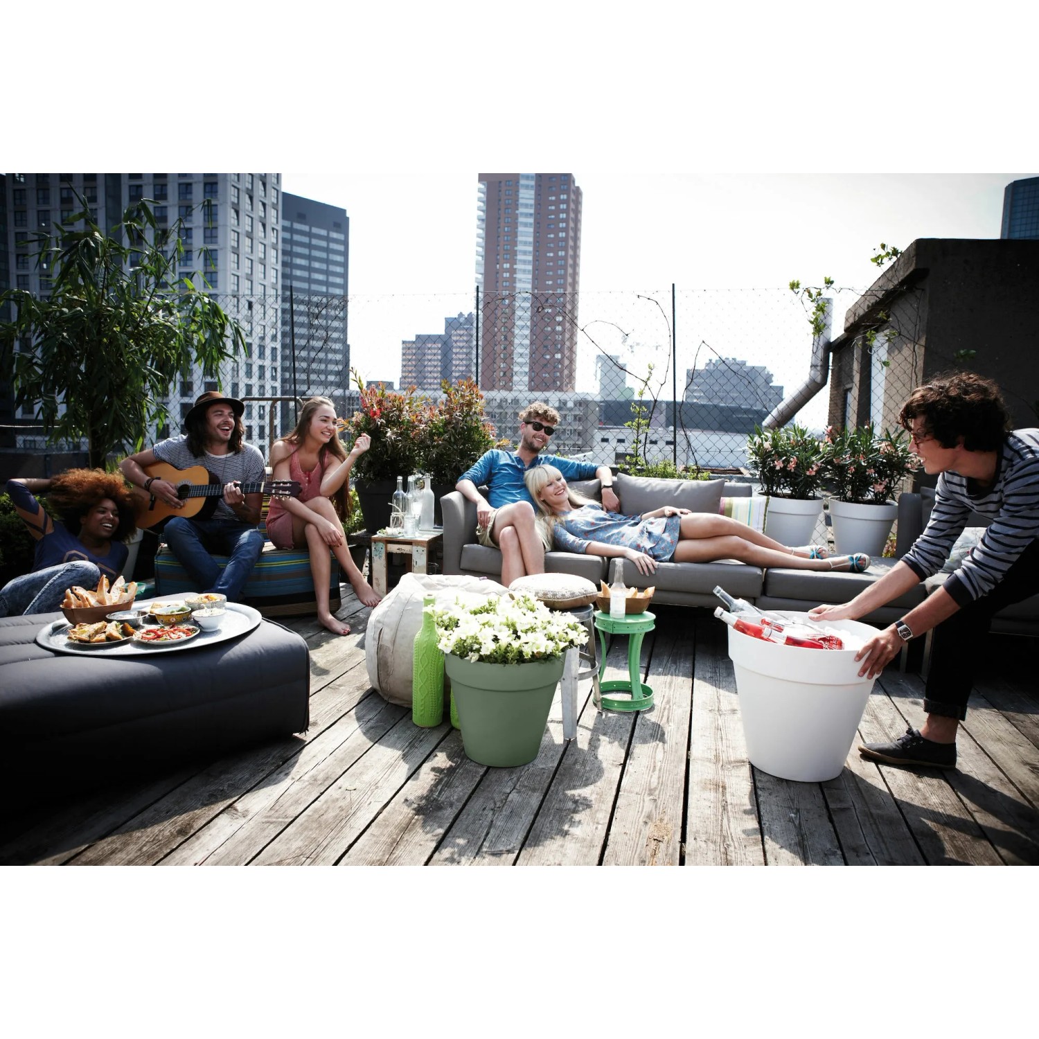 Elho Blumentopf Loft Urban, pistaziengrün, mit Rollen, auf einer Dachterrasse mit entspannten Menschen.