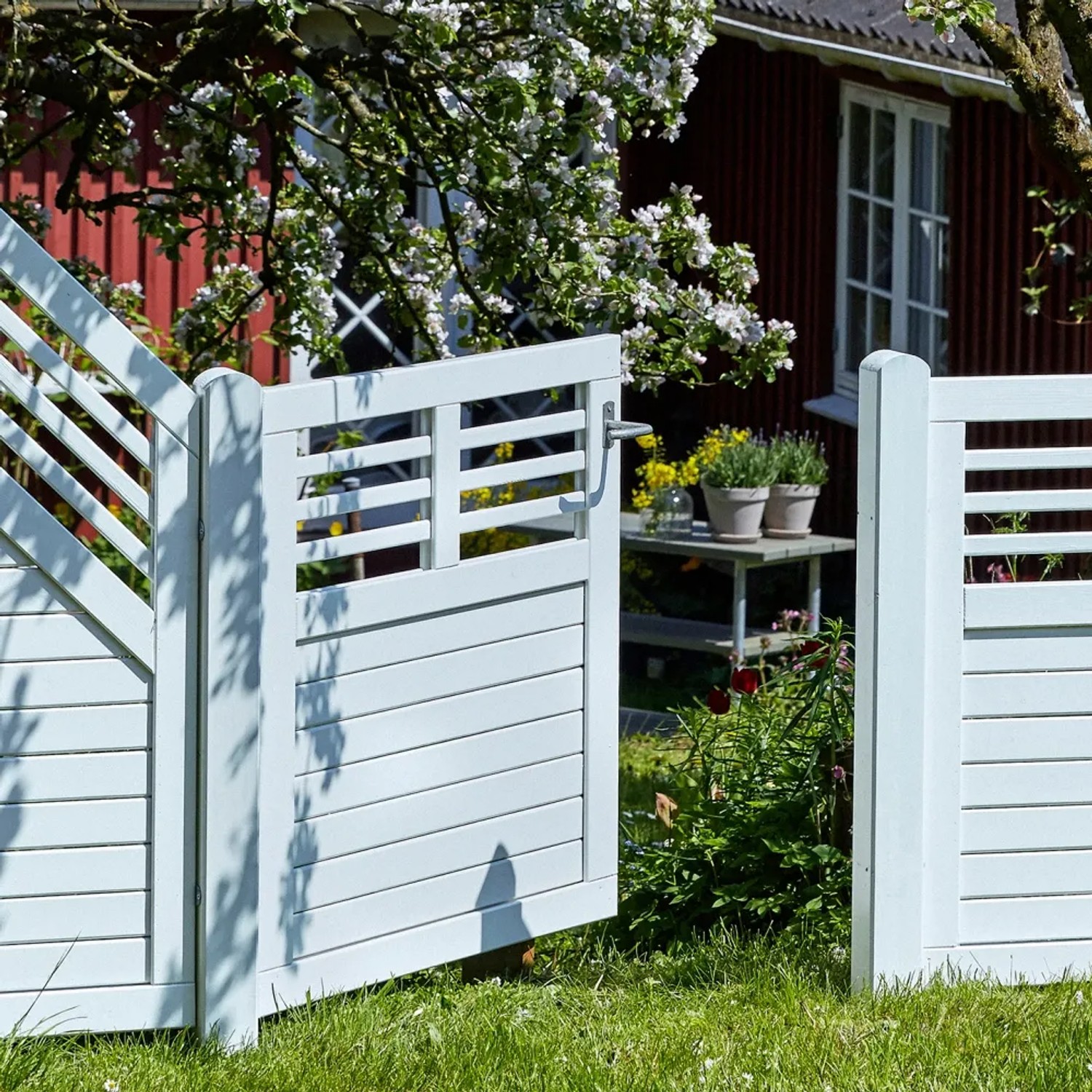 Offenes, weißes Gartentor Decora aus Nadelholz, 100x95 cm, vor einem Garten mit Haus.