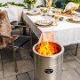 Feuerhand Pyron Feuertonne aus Edelstahl, 25 l, mit brennendem Holz vor gedecktem Tisch im Garten.
