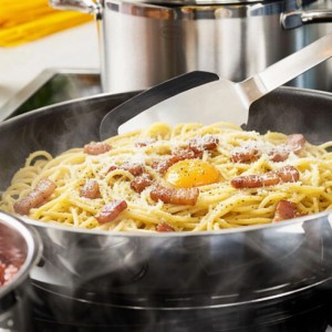 RÖSLE Servierpfanne aus Edelstahl mit Keramikbeschichtung, gefüllt mit dampfenden Spaghetti Carbonara, wird zubereitet.