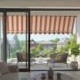 Spettmann Fallarmmarkise Line, weiß/gelb-orange-rot, auf Balkon mit Möbeln.