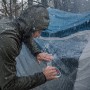 Mann repariert Zelt mit transparentem Tesa Ultra Power Clear Reparaturband bei Regen.